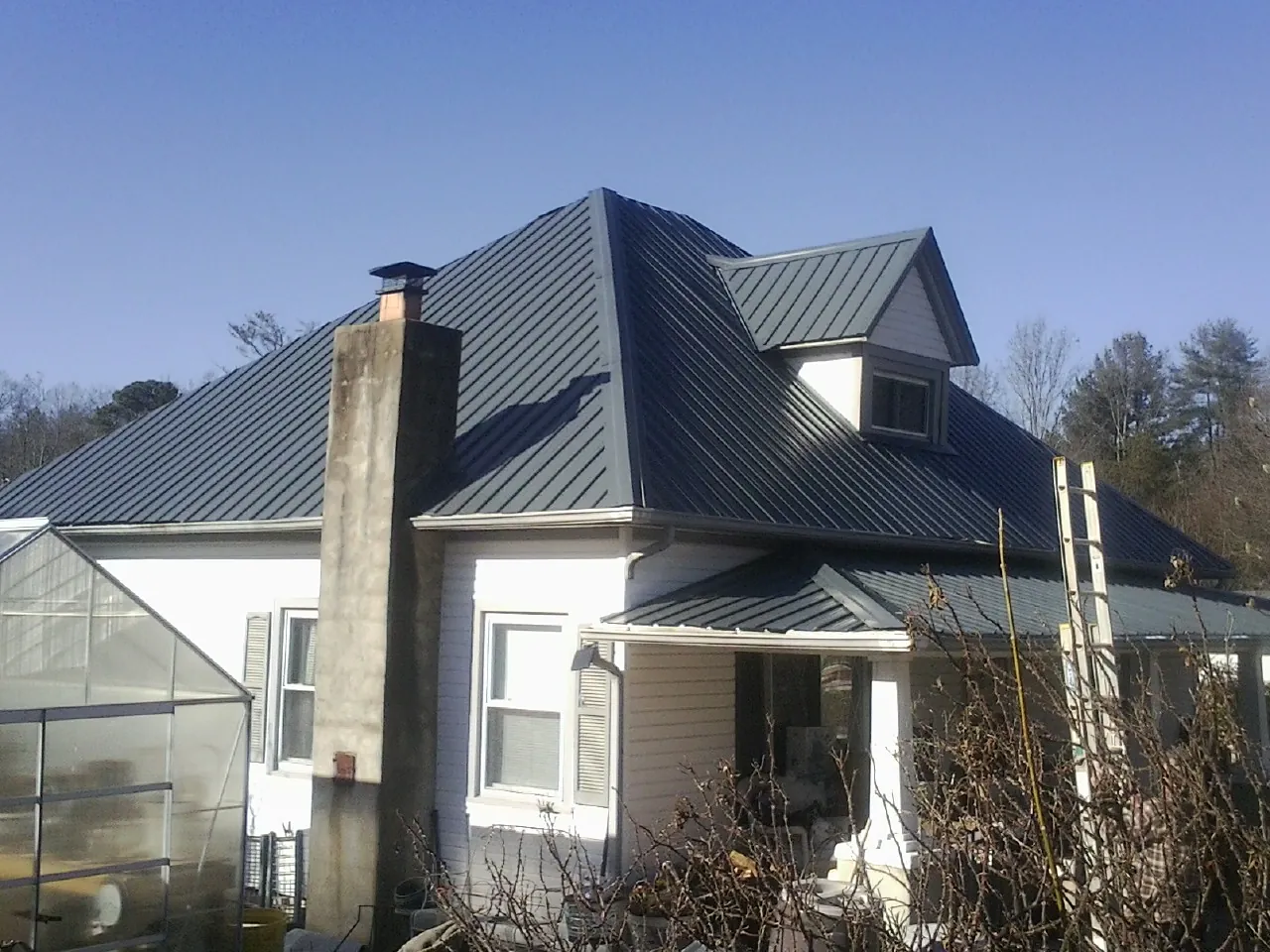 Dark blue standing seam metal roof on a white farmhouse with dormer — Slate & Tile Roof Repair by Roofing Brothers in Elmo