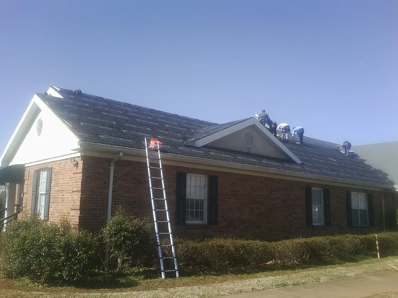 Crew tearing shingles off a brick ranch roof with a ladder set — Emergency Roof Repair work by our crew in Elmo