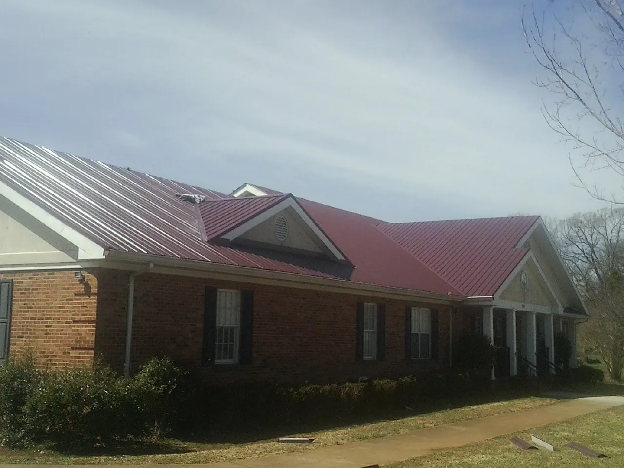Red metal roof with gabled entries on a long brick building, from a Hail Damage Roof Repair job in Elmo