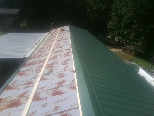 Old rusted panels beside newly installed green metal roofing — Wind Damage Roof Repair by Roofing Brothers in Elmo