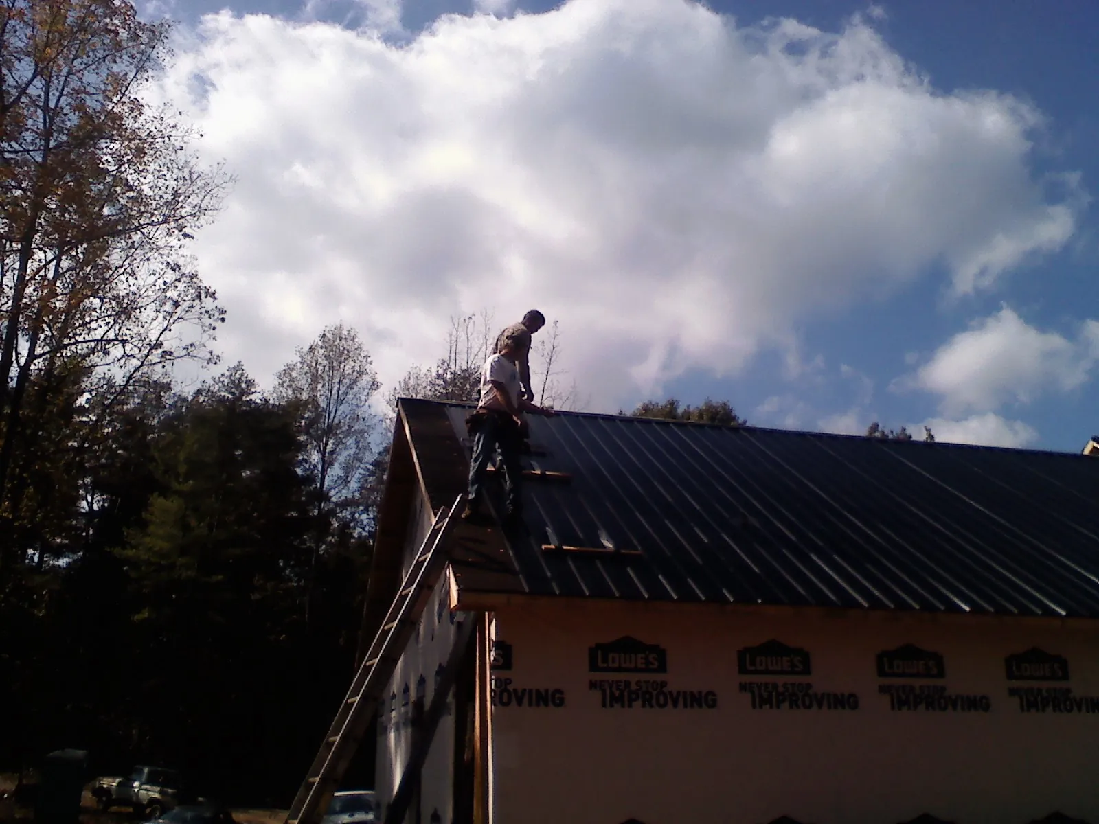 Roofer fastening dark metal panels high against a cloudy sky, from a Roof Inspection job in Elmo