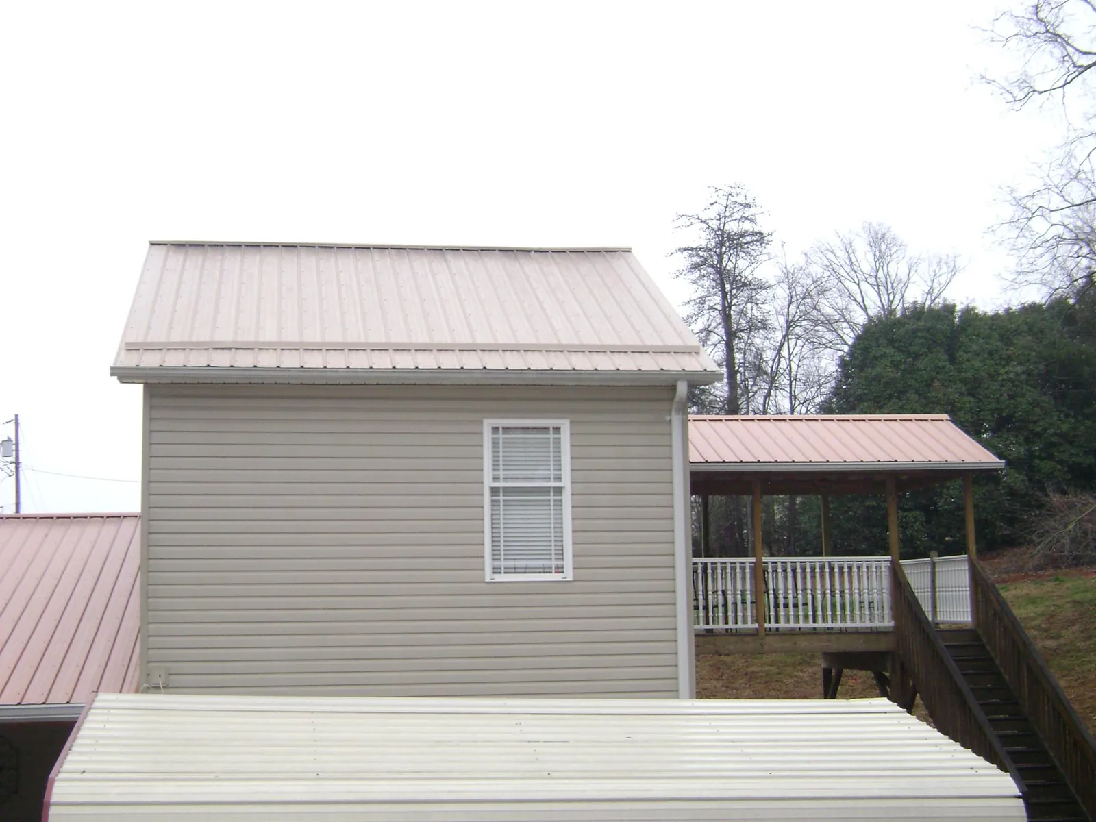 Tan metal roofs on a two story addition and attached porch, from a Roof Replacement job in Elmo